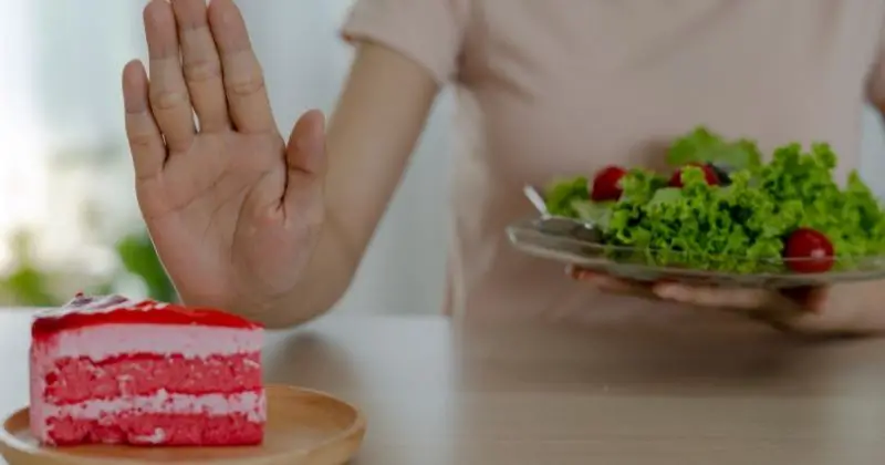 How to Stop Eating Sugar – a woman with a salad turning down a piece of cake.