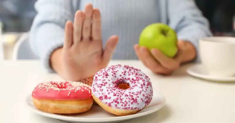 Foods to Avoid for Prediabetics - a woman with an apple and turning down a doughnut.